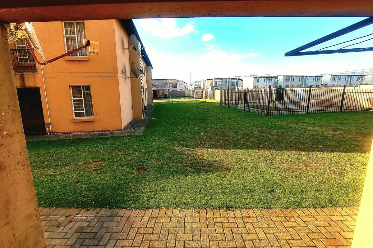 View of a communal garden area and apartment building exterior, featuring paved patio space and perimeter fencing.