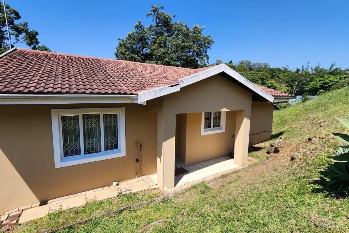 Rear exterior view of the townhouse featuring a tiled roof, covered patio area, and security-fitted windows set against a sloped garden.