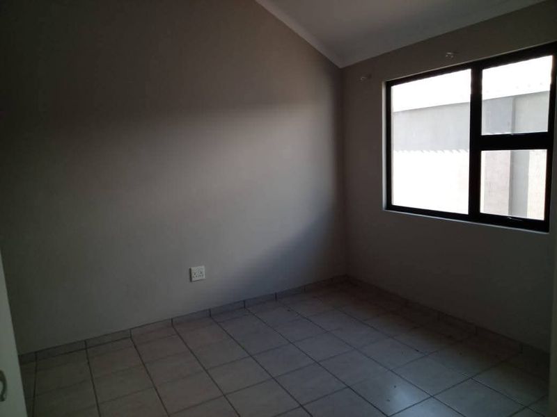 A vacant bedroom featuring neutral wall tones, tiled flooring, and a large aluminium-framed window providing natural light.