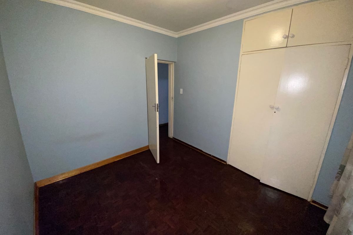 An empty bedroom featuring parquet flooring, built-in cupboards, and blue painted walls with crown molding.