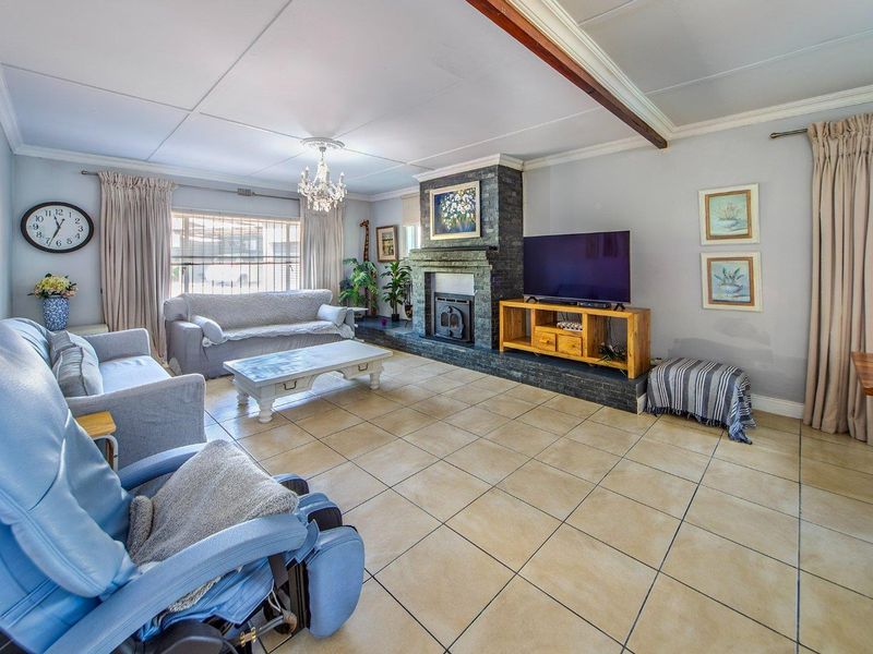 Spacious living room featuring tiled flooring, a prominent stone-clad fireplace, and an exposed ceiling beam, offering a comfortable and functional family space.