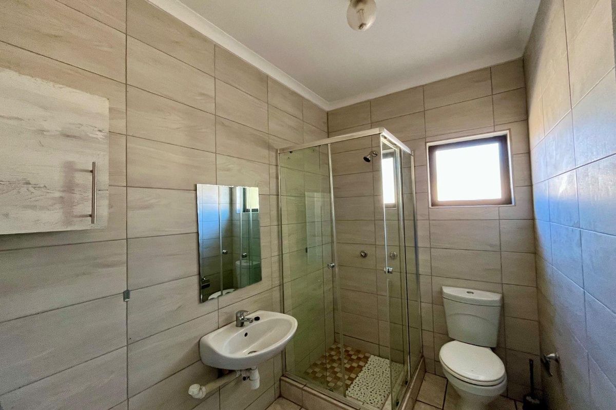 A compact bathroom featuring floor-to-ceiling neutral tiling, a glass-enclosed shower, a wall-mounted basin, and a standard toilet.