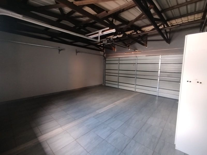 A spacious, clean, and well-maintained double garage featuring tiled flooring, exposed roof trusses, and an automated sectional garage door.
