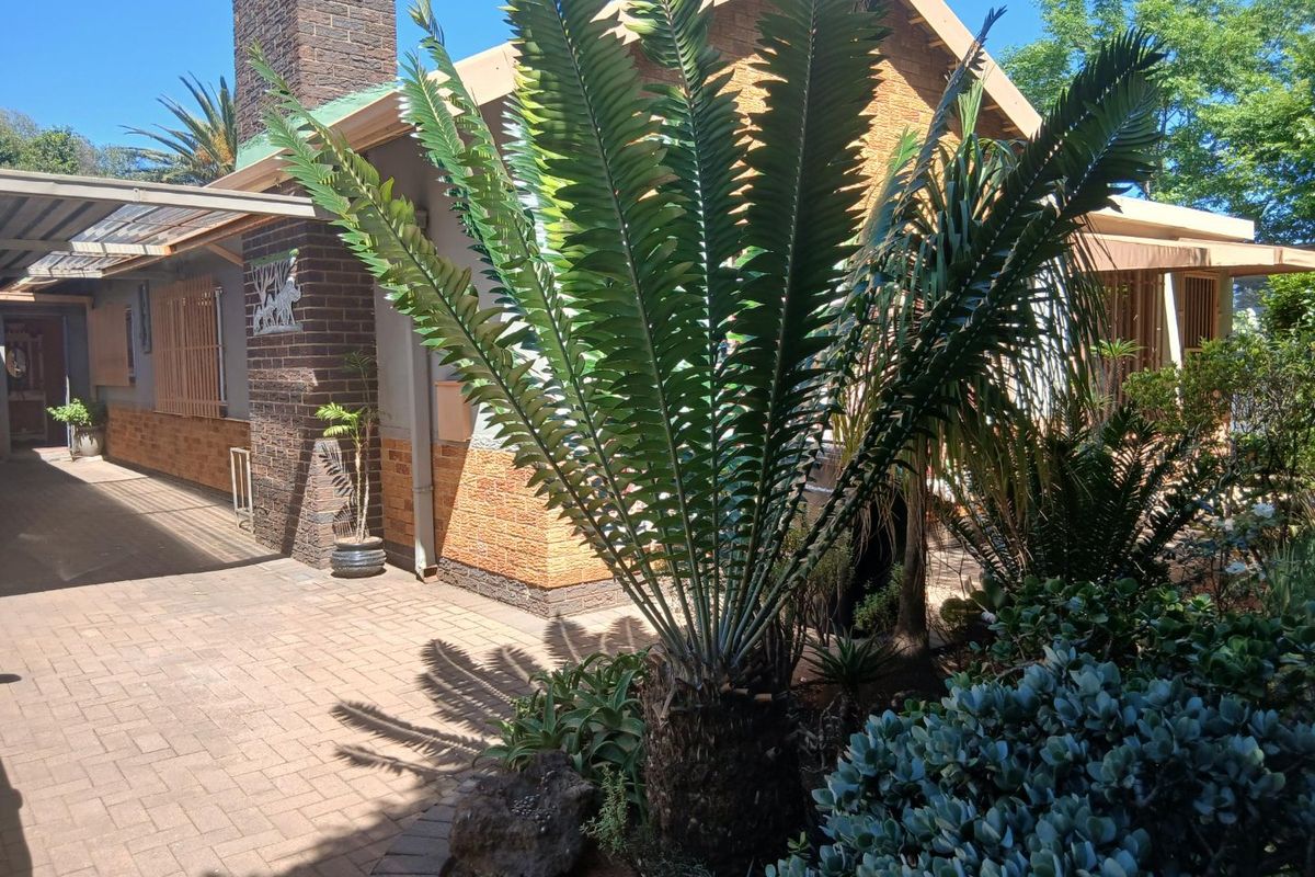 A rear exterior view of the house featuring a paved patio area, brick chimney, and established garden landscaping.