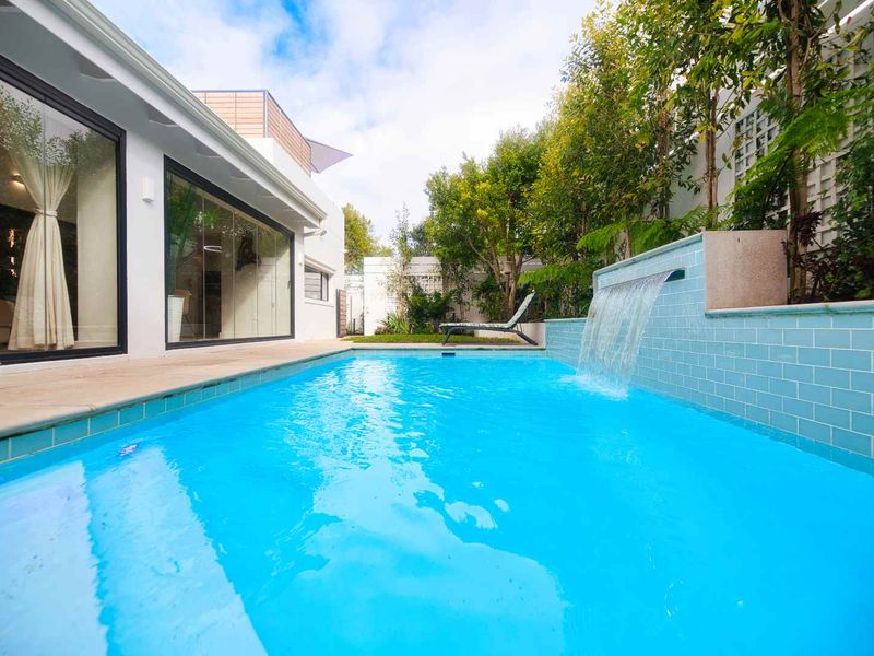 A well-maintained swimming pool area featuring a modern water feature, tiled surround, and direct access to the home through large sliding glass doors.