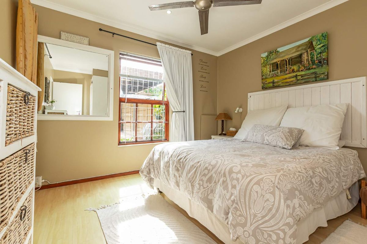 A cozy bedroom featuring laminate flooring, a ceiling fan, and a window with security bars, offering a comfortable and functional living space.