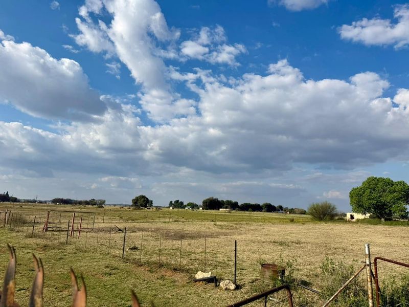 Expansive open farm land featuring natural grass fields and perimeter wire fencing under a clear blue sky.