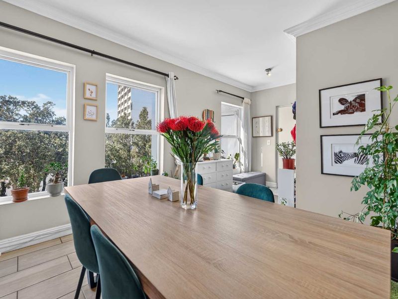 A bright and well-maintained dining area featuring tiled flooring, decorative cornicing, and large windows that provide ample natural light.