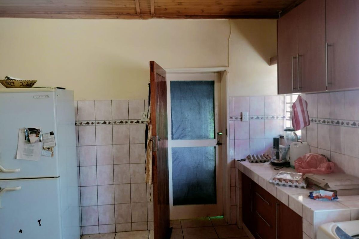 A functional kitchen featuring tiled countertops, built-in cabinetry, and a timber ceiling, providing a practical workspace with direct access to an exterior door.