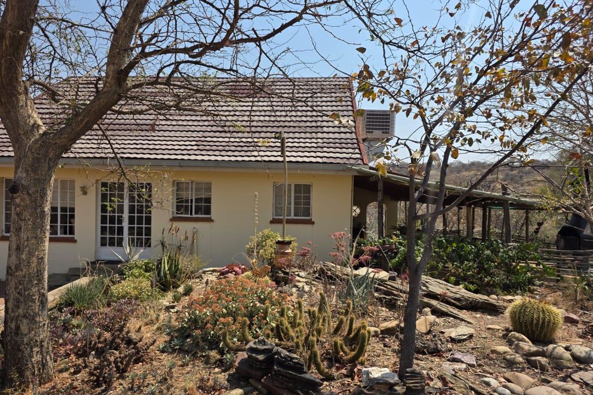 Rear view of the house featuring a tiled roof, french doors, and a covered patio area set within a landscaped garden.