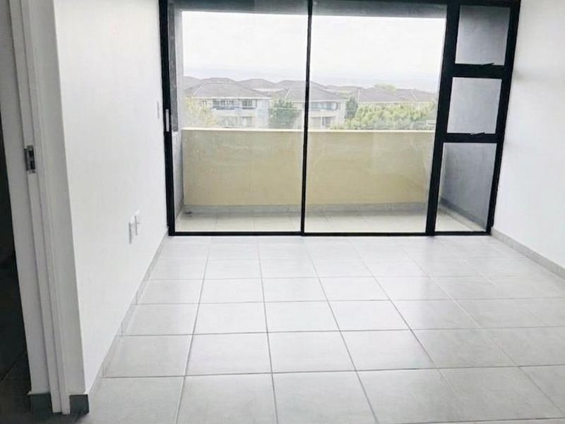 A bright, empty bedroom featuring neutral tiled flooring and a large sliding glass door providing access to a private balcony.