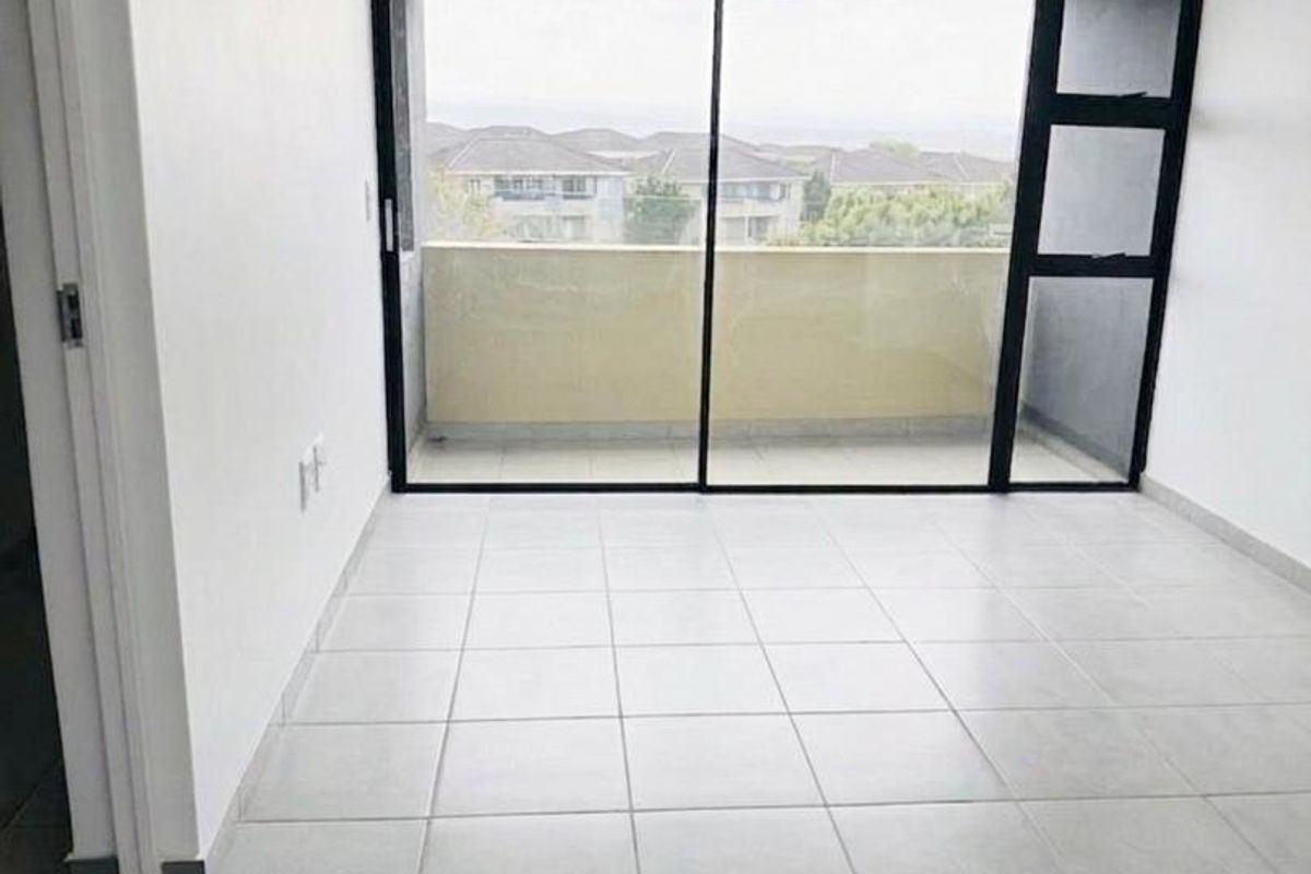 A bright, empty bedroom featuring neutral tiled flooring and a large sliding glass door providing access to a private balcony.