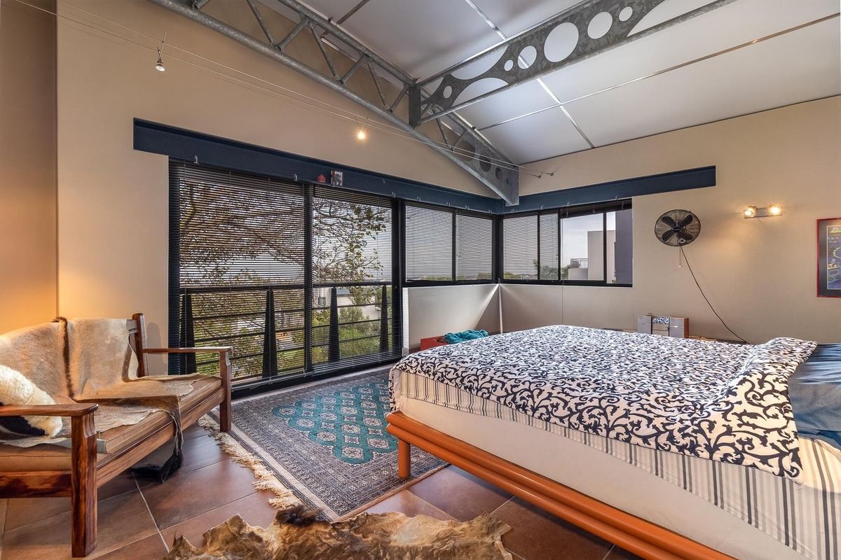 Spacious bedroom featuring high vaulted ceilings with exposed steel trusses, large windows with integrated blinds, and tiled flooring.