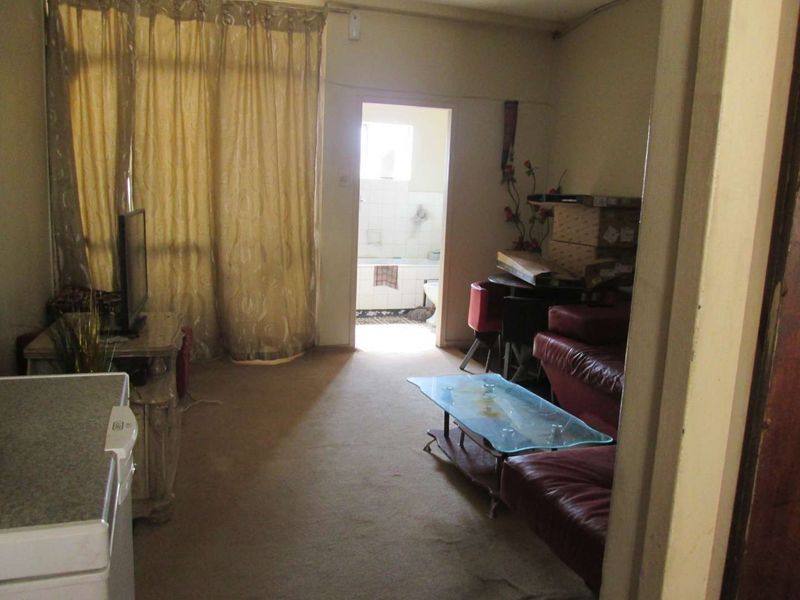 A living room area featuring carpet flooring and access to an adjacent bathroom, currently showing signs of wear and dated finishes.