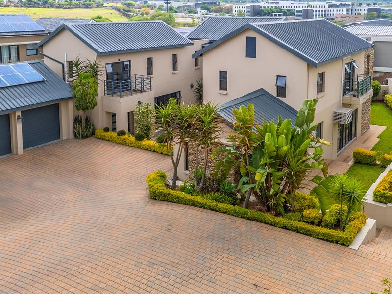 Aerial view of a modern residential property featuring a paved driveway, multiple garage bays, solar panels, and well-maintained landscaped garden areas.