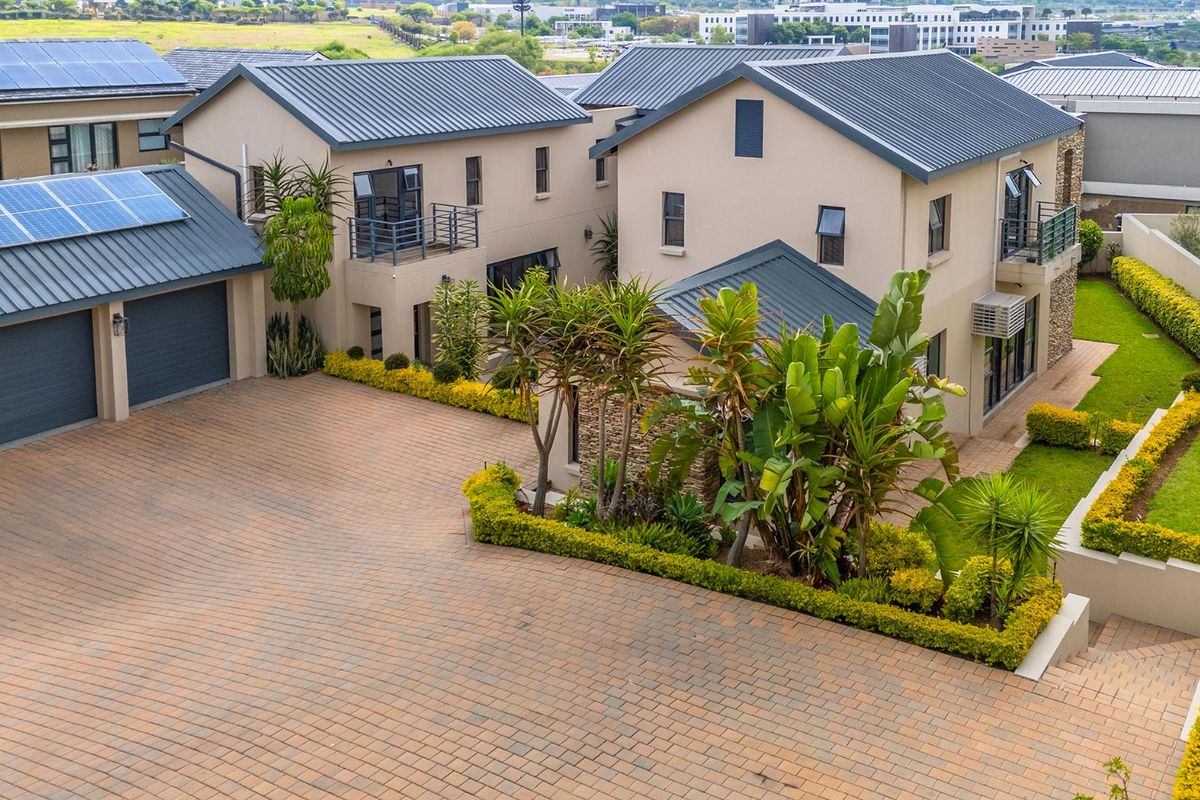 Aerial view of a modern residential property featuring a paved driveway, multiple garage bays, solar panels, and well-maintained landscaped garden areas.