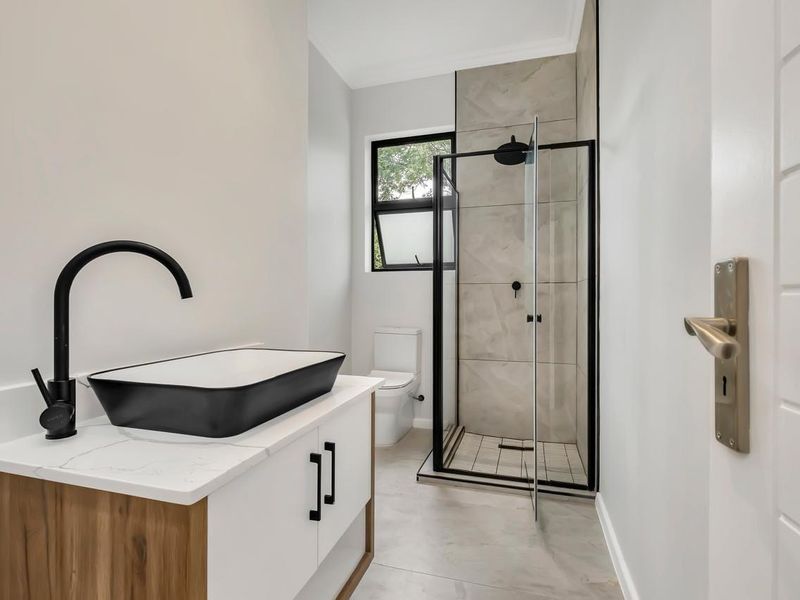 Modern bathroom featuring a contemporary vanity with vessel sink, black fixtures, and a walk-in shower with neutral tiling.