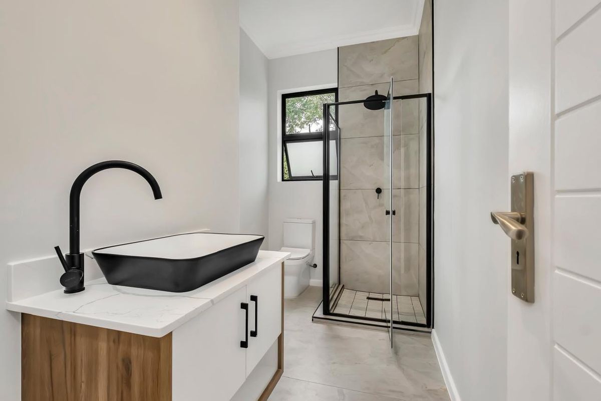 Modern bathroom featuring a contemporary vanity with vessel sink, black fixtures, and a walk-in shower with neutral tiling.