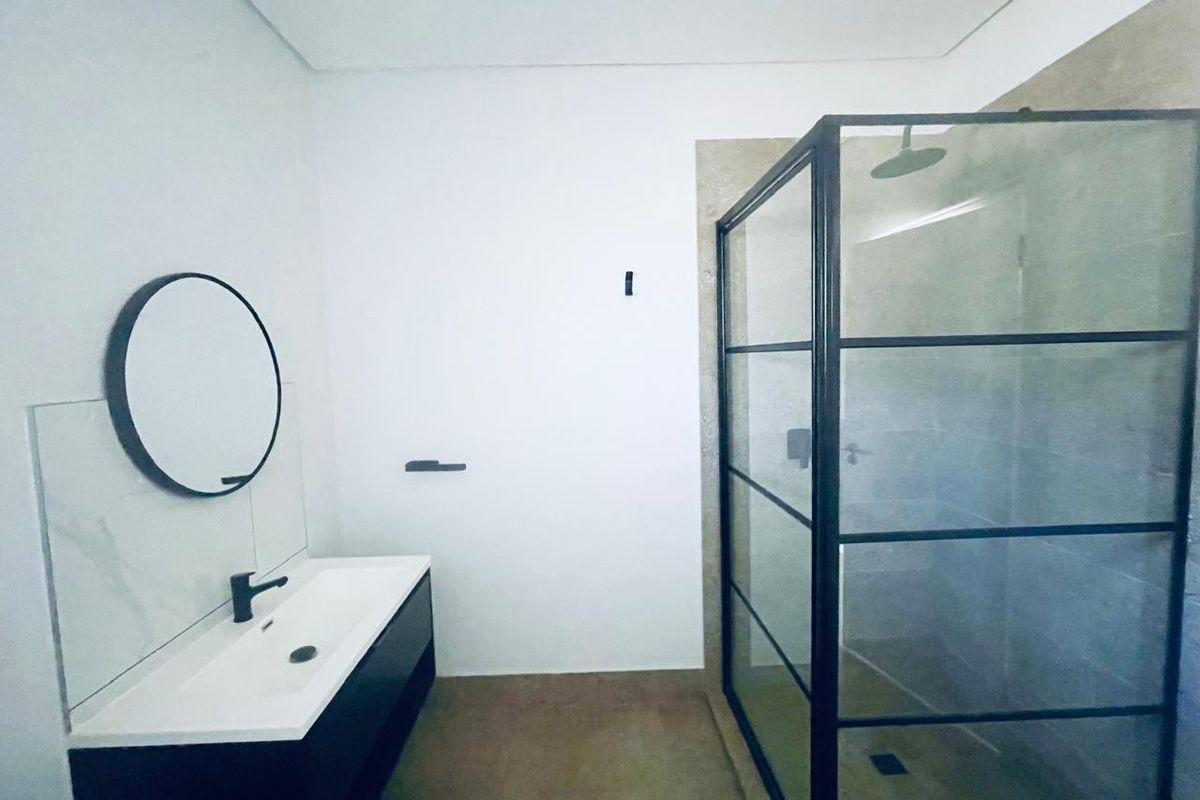 Modern bathroom featuring a sleek vanity with basin, black fixtures, and a spacious walk-in shower with a black-framed glass enclosure.