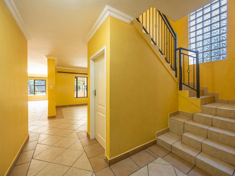 Bright entrance hall featuring a tiled staircase with wrought iron balustrade, glass block feature window, and neutral tiled flooring leading into the living area.