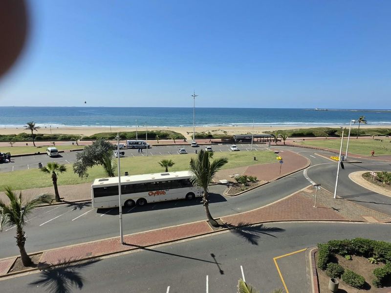 Elevated view overlooking the coastal beachfront, public parking area, and surrounding landscaped grounds.