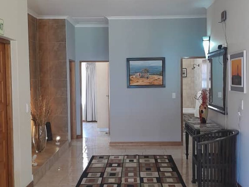 A spacious tiled hallway featuring neutral wall tones, coving, and wall-mounted lighting, providing access to adjacent rooms.