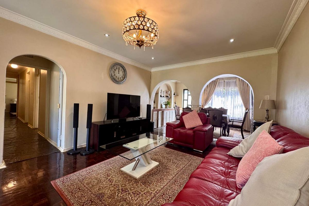 Spacious living room featuring polished timber flooring, decorative ceiling cornices, and arched entryways leading to the dining area.
