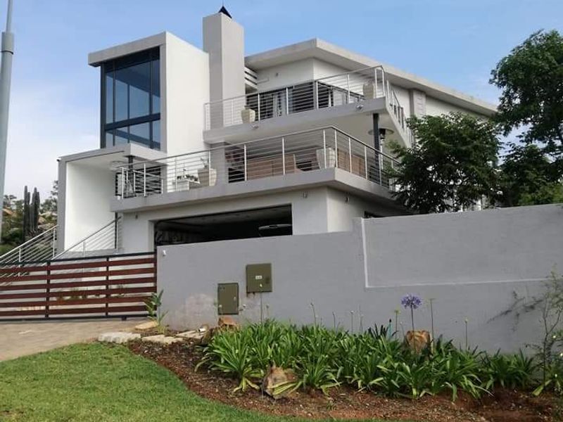 Modern multi-level residential property featuring clean architectural lines, expansive glass windows, multiple balconies with stainless steel railings, and a secure boundary wall.