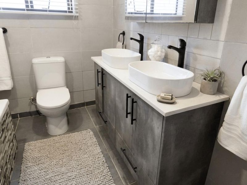 Modern bathroom featuring a double vanity with vessel sinks, matte black fixtures, tiled walls and flooring, and a bathtub.