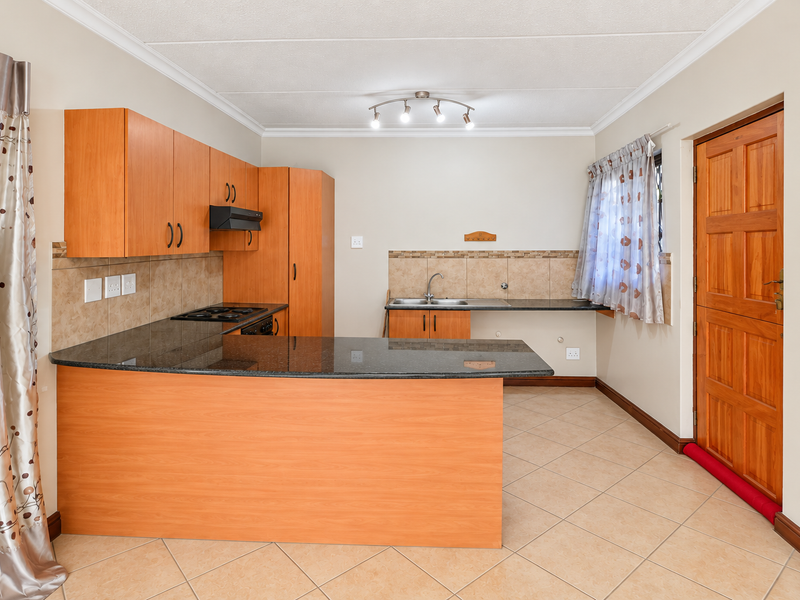 A functional kitchen featuring laminate cabinetry, granite countertops, a built-in hob with extractor, and tiled flooring, providing a clean and practical workspace.