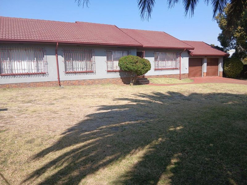Front view of a single-story house featuring a tiled roof, brick plinth, security bars on windows, and a double garage with a paved driveway.