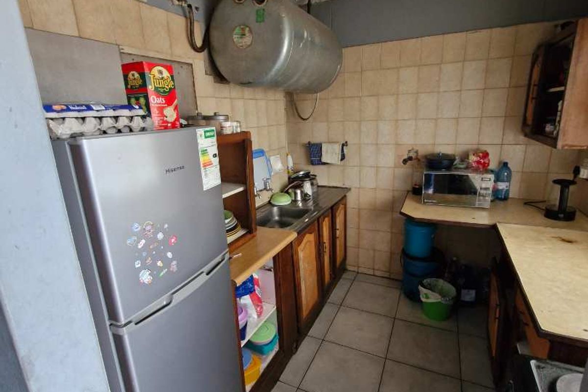 A compact kitchen featuring tiled flooring, built-in cabinetry, a sink, and an exposed wall-mounted water heater tank.