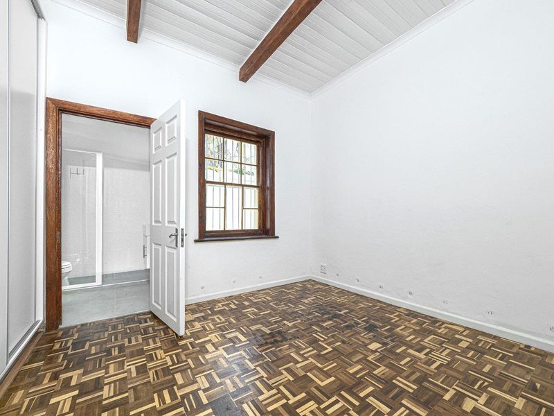 An empty bedroom featuring classic parquet flooring, exposed timber ceiling beams, and an en-suite bathroom access.