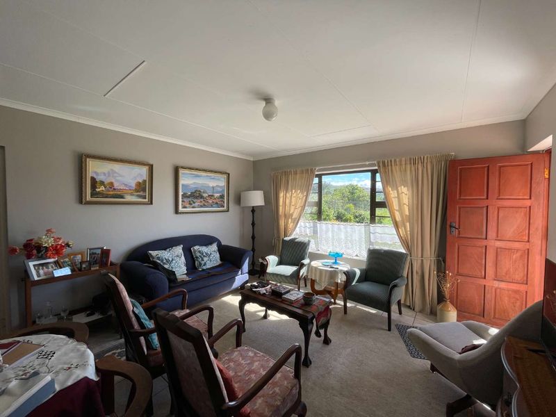 A comfortable living room featuring carpeted flooring, a large window with natural light, and a solid timber door leading to the exterior.