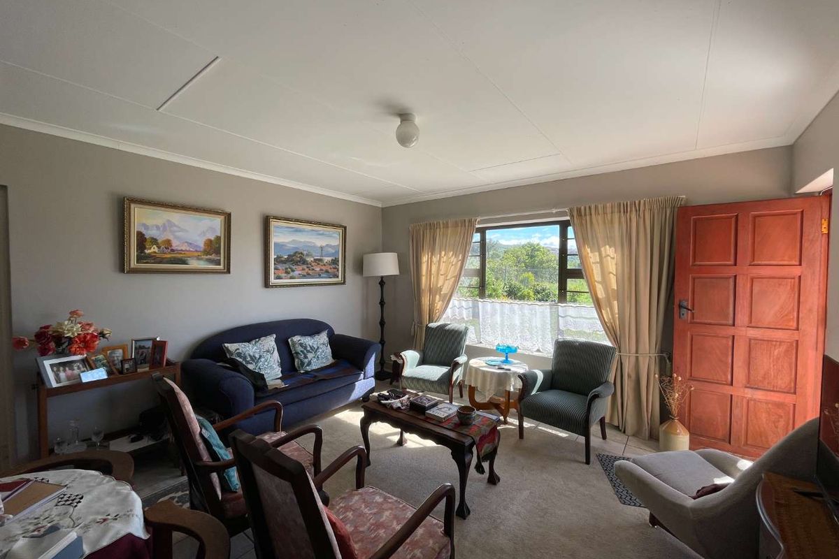 A comfortable living room featuring carpeted flooring, a large window with natural light, and a solid timber door leading to the exterior.