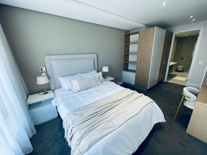 A modern, well-maintained bedroom featuring neutral tones, built-in cabinetry, recessed lighting, and an adjoining en-suite bathroom.