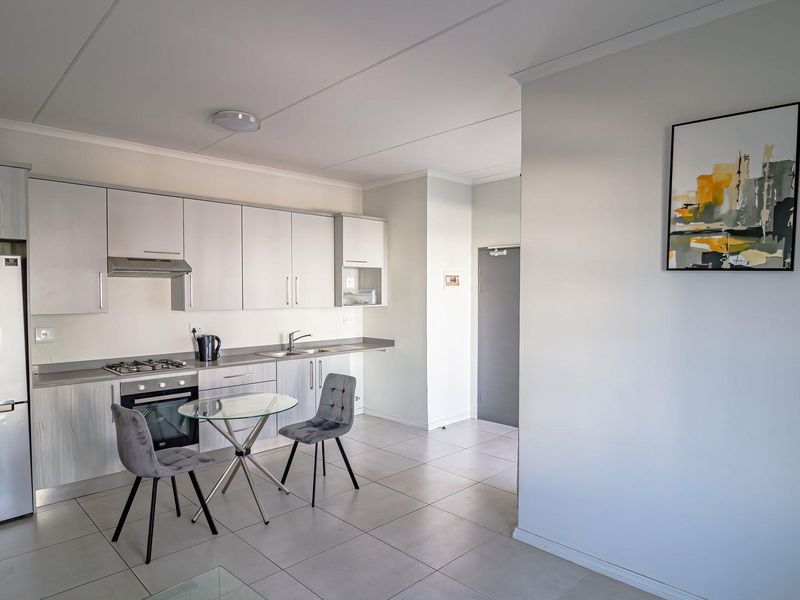 Modern open-plan kitchen featuring light-toned cabinetry, integrated appliances, and tiled flooring, seamlessly flowing into the adjacent living area.