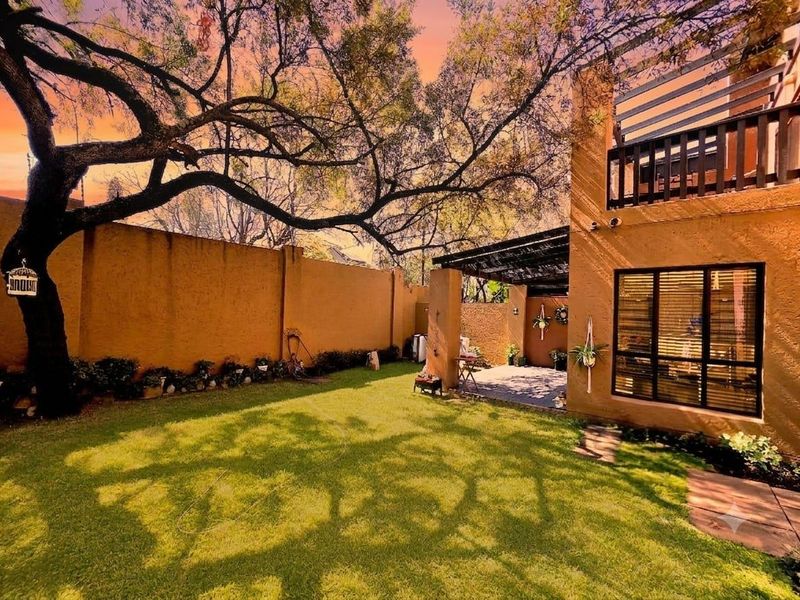 A private rear garden featuring a well-maintained lawn, a paved patio area with a pergola, and a balcony overlooking the outdoor space.