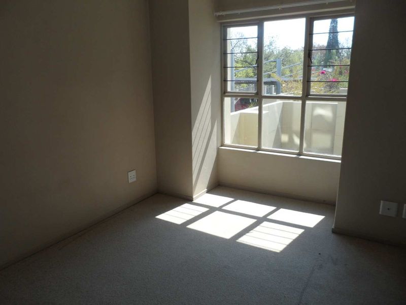 An empty bedroom featuring carpeted flooring, large windows with security bars, and natural light, providing a blank canvas for personalization.
