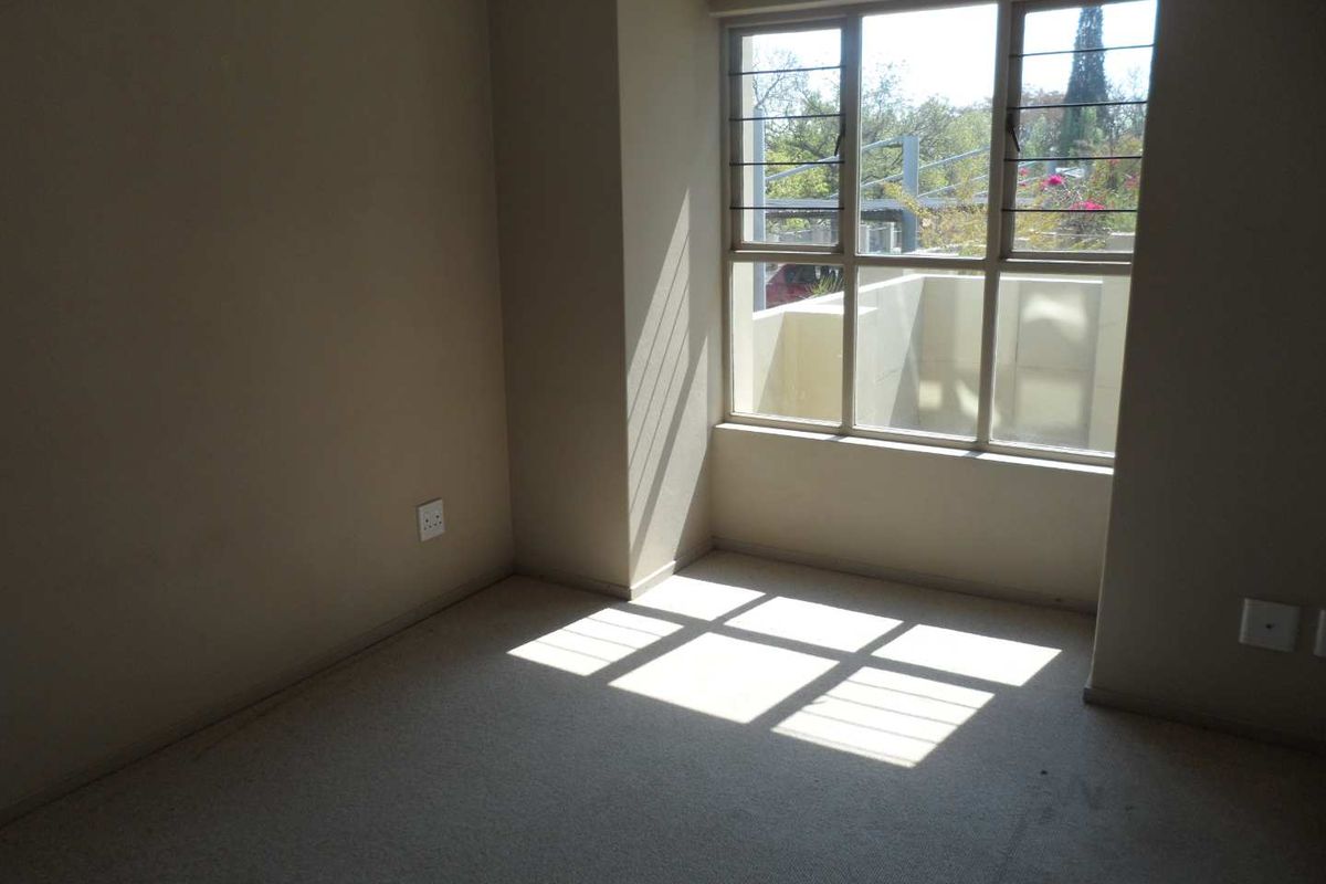 An empty bedroom featuring carpeted flooring, large windows with security bars, and natural light, providing a blank canvas for personalization.