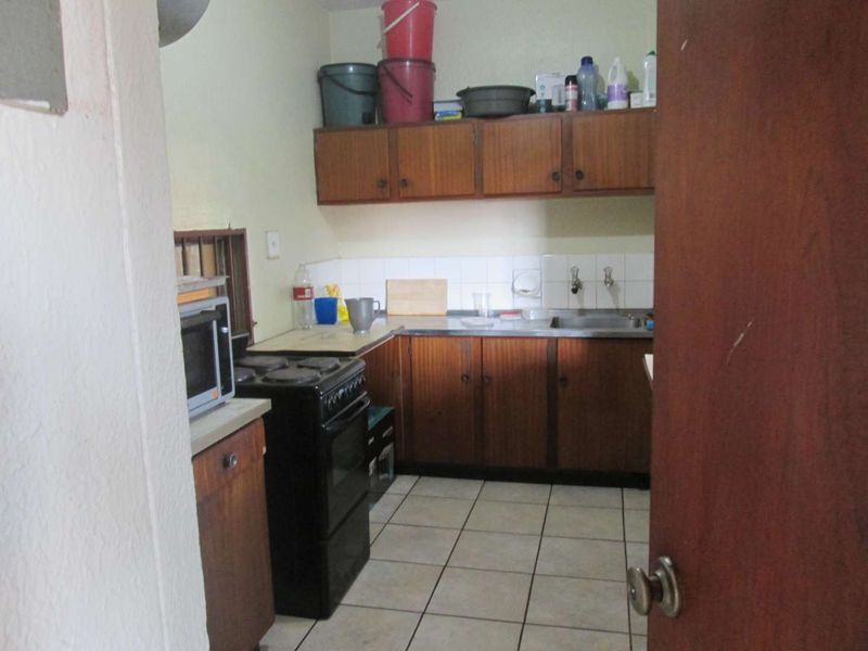 A dated kitchen featuring laminate cabinetry, a stainless steel sink, tiled backsplash, and ceramic floor tiles, offering potential for a modern renovation.