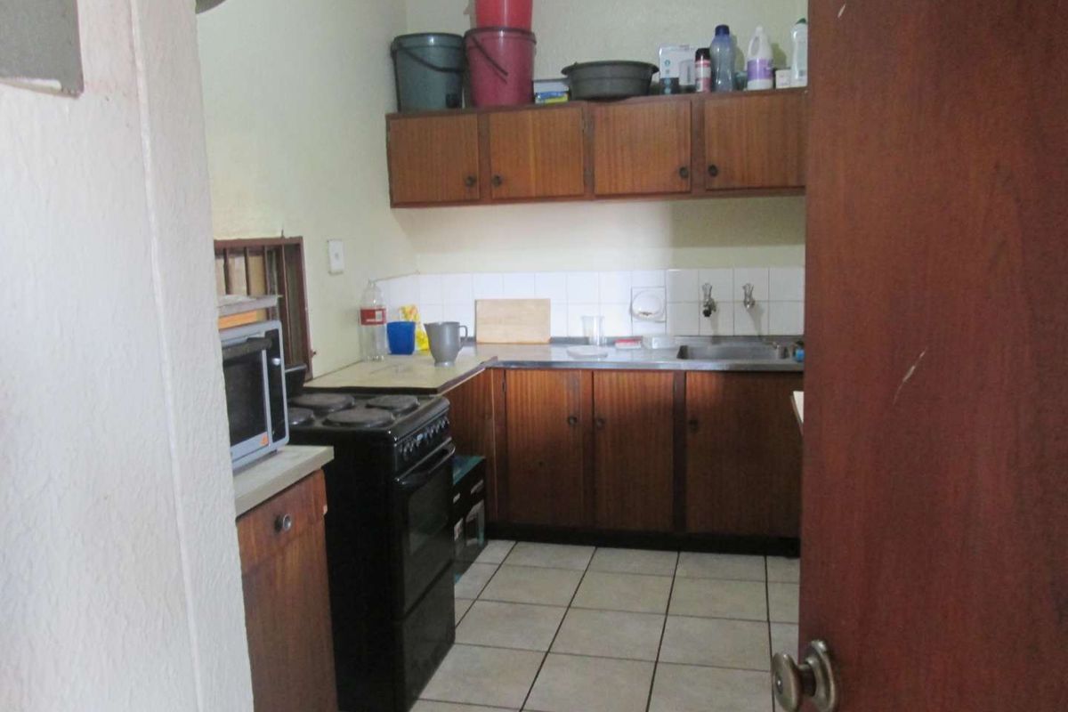 A dated kitchen featuring laminate cabinetry, a stainless steel sink, tiled backsplash, and ceramic floor tiles, offering potential for a modern renovation.