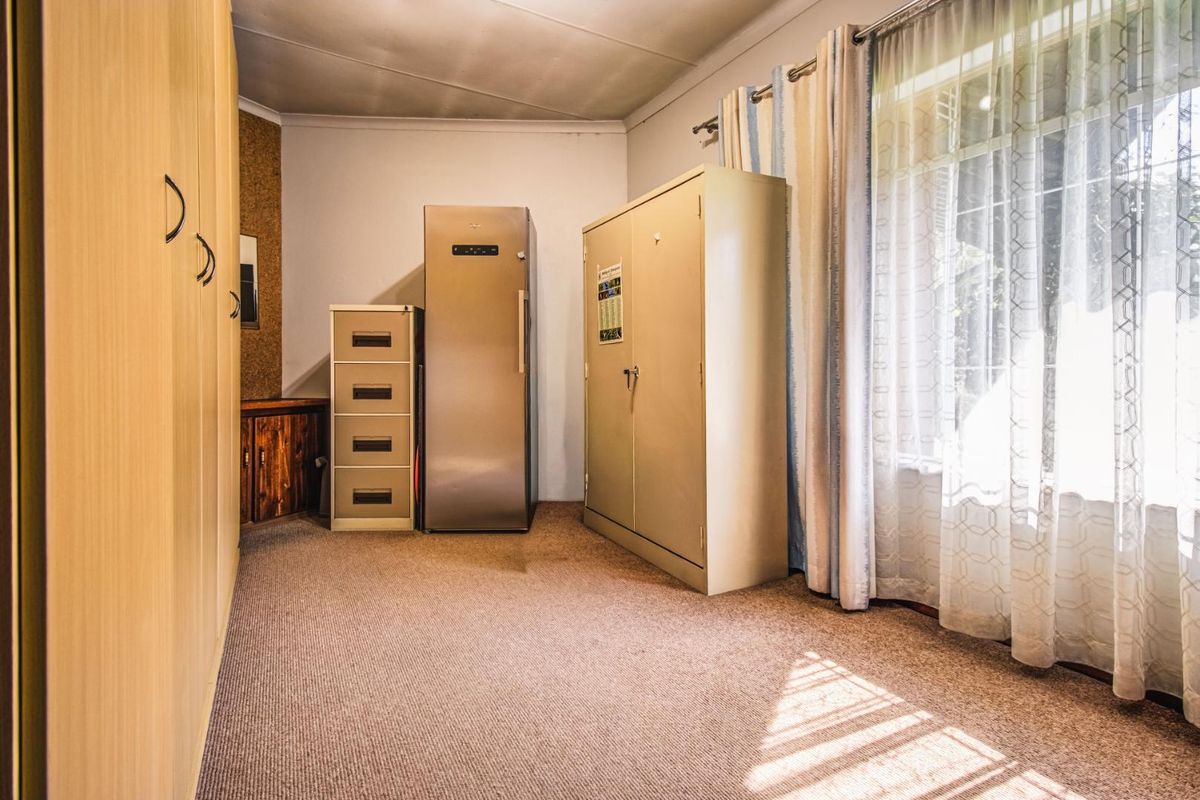 A functional bedroom or utility space featuring built-in wooden cabinetry, carpeted flooring, and a large window with curtains.
