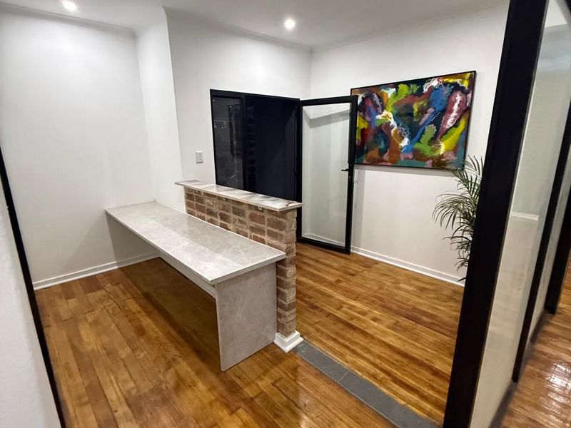 Modern office space featuring polished hardwood floors, a unique exposed brick partition with a stone-topped desk, and sleek glass-panelled entry doors.