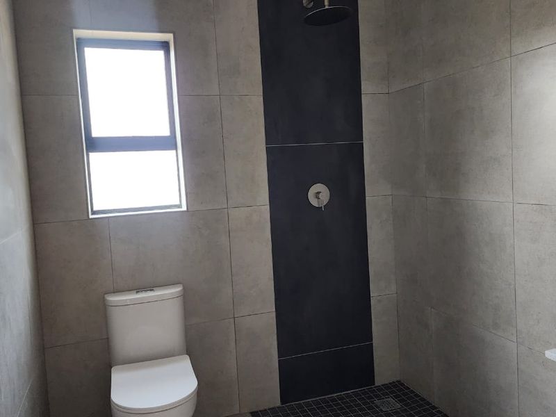 Modern bathroom featuring large format grey wall tiles, a dark accent shower wall, a walk-in shower area, and a contemporary toilet.