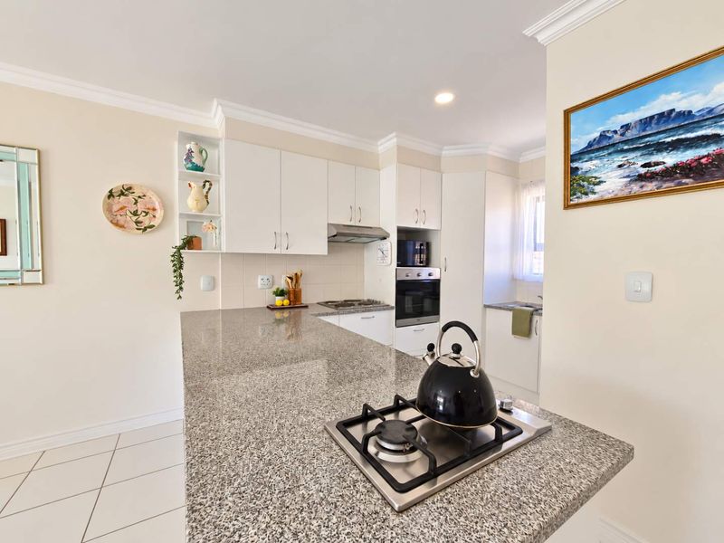 A well-maintained kitchen featuring granite countertops, a built-in oven, gas hob, and ample cabinetry, offering a functional and clean cooking space.