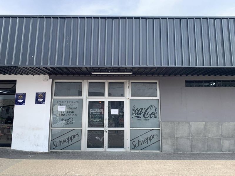 Front facade of a retail property featuring a metal awning, glass storefront entrance, and paved walkway.
