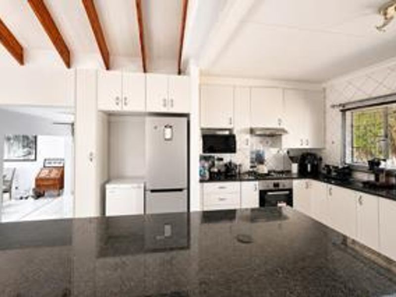 A well-appointed kitchen featuring granite countertops, built-in cabinetry, a gas hob with extractor, and distinctive exposed timber ceiling beams.