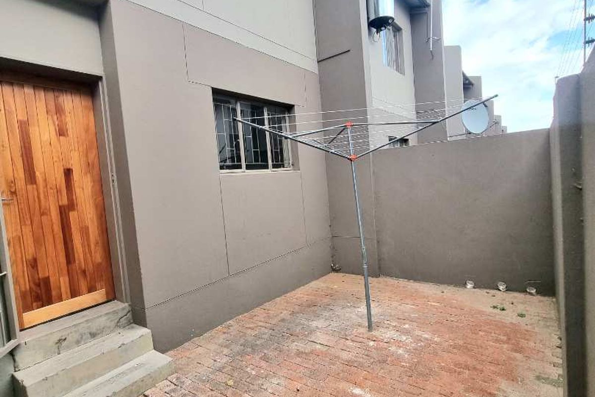 A private rear courtyard featuring brick paving, a solid wood entrance door, and a wall-mounted solar geyser unit on the exterior facade.