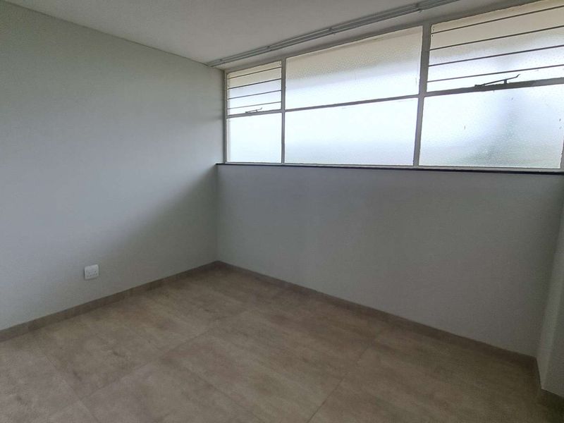 An empty bedroom featuring neutral tiled flooring and large louvered windows providing natural light.